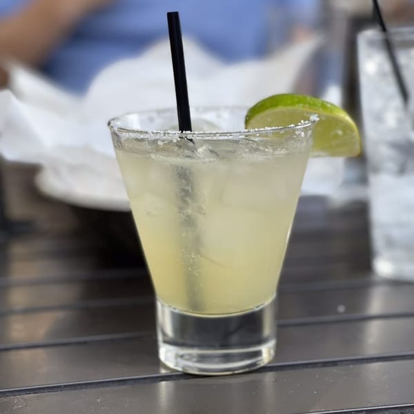 A refreshing margarita with a salted rim, lime wedge, and black straw on a metal table.
