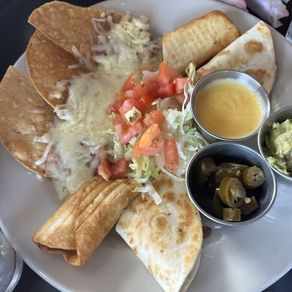 A Mexican platter with nachos, quesadillas, a flauta, and sides of salsa, guacamole, and jalapeños.