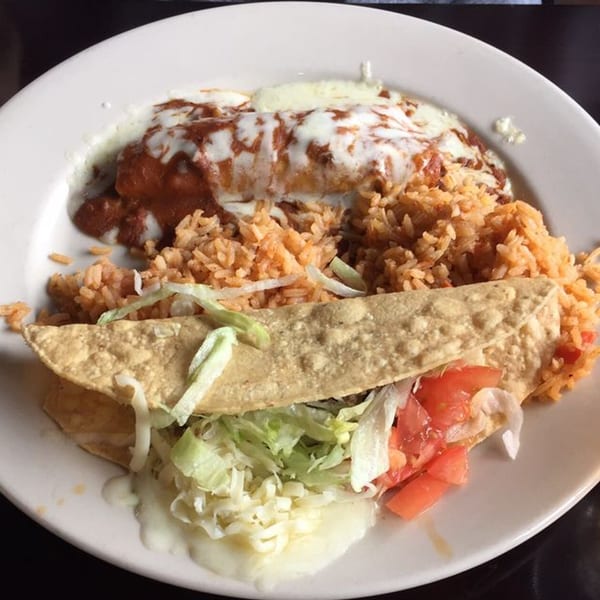 A plate of Mexican food with a cheesy burrito, rice, and a taco with lettuce and tomatoes.