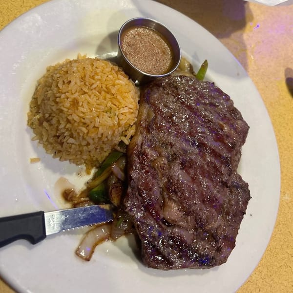 Grilled steak, Mexican rice, and a side of sauce with sautéed vegetables on a white plate.